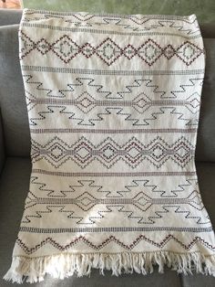 a white and red blanket sitting on top of a couch next to a gray sofa