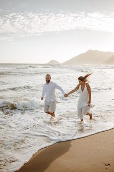 a man and woman holding hands walking into the ocean