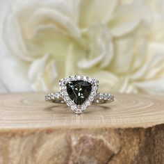 a pear shaped diamond ring on top of a piece of wood with flowers in the background