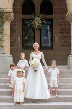 a woman in a wedding dress standing with her children on the steps and holding hands