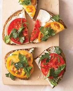 four slices of bread with tomatoes, cheese and herbs on them sitting on a cutting board