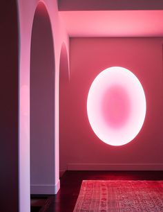 a room with pink lighting and a rug on the floor in front of an archway