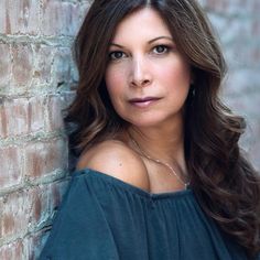 a woman leaning against a brick wall with her hand on her hip and looking at the camera