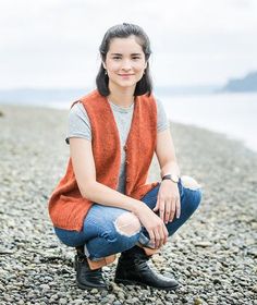 a woman is sitting on the beach with her legs crossed and looking at the camera