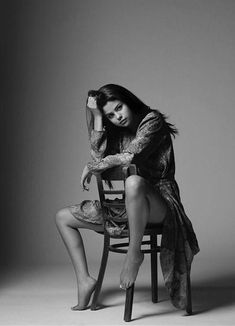 a woman sitting on top of a wooden chair in a black and white photo with her legs crossed