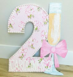 the number two is decorated with flowers and a pink bow as well as a glass of champagne