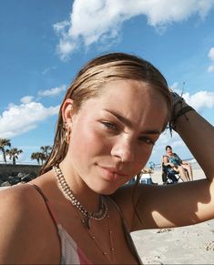 a young woman is posing on the beach with her hands behind her head and people in the background