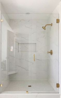 a white shower with gold fixtures and marble tile flooring in the shower stall area