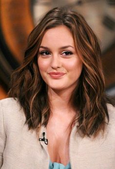 a close up of a person wearing a suit and smiling at the camera with a clock in the background