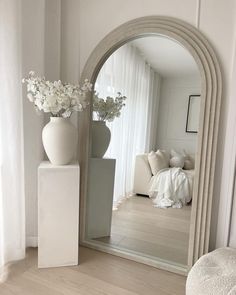 a white vase with flowers sitting on top of it next to a mirror in a room