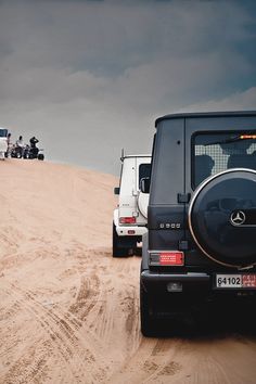 jeeps are parked in the sand on a cloudy day with motorcyclists behind them