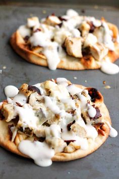 two flatbread pizzas with chicken, cheese and ranch dressing on top sitting on a baking sheet