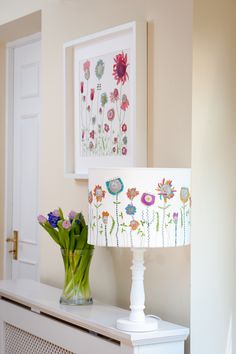 a vase with flowers sitting on top of a white table next to a lamp shade