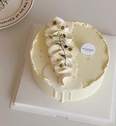 a white cake sitting on top of a box next to a cup and saucer