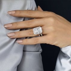 a woman's hand with a diamond ring on her finger, wearing a silver dress