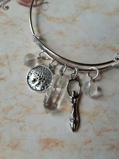 This cute silver-toned metal expandable charm bangle was made with Lammas, or Lughnasadh, in mind. It matches a Lammas themed prayer bead strand I recently made. It would also match most anything else, as well, since the stones used are clear. It's made with a silver-toned metal expandable bangle and features a gemstone point, silver-toned metal charms, and bead dangles. In the center is a small bullet-shaped clear Quartz pendulum point. It has two silver-toned metal charms. One is a Goddess and Spiritual Nickel-free Charm Bracelet As Gift, Spiritual Nickel-free Charm Bracelet For Gifts, Nickel-free Spiritual Charm Bracelet As A Gift, Silver Adjustable Crystal Bracelet For Meditation, Spiritual Charm Bangle Bracelet, Silver Spiritual Crystal Bracelet For Healing, Silver Bangle For Meditation, Spiritual Charm Bracelet With Dangling Charms, Spiritual Sterling Silver Charm Bracelet