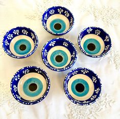 four blue and white bowls sitting on top of a white tablecloth with an eyeball in the center