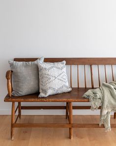 a wooden bench with two pillows on it and a blanket draped over the backrest