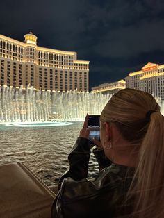 a woman taking a photo with her cell phone in front of the fountains of water