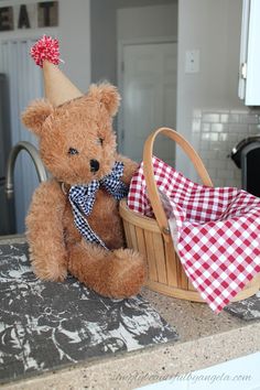 a brown teddy bear sitting on top of a counter next to a basket filled with cloth