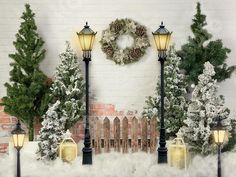 a christmas scene with snow on the ground and street lights in front of a brick wall