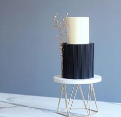 a three tiered cake with black and white frosting on a marble stand against a blue wall