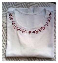 a white t - shirt with red embroidery on the chest and neckline is laying on a bed