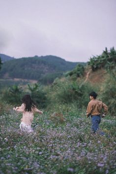 two people walking through a field with purple flowers