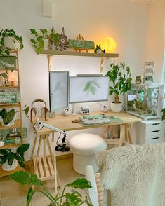 a desk with two computer monitors on top of it next to a chair and potted plants