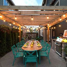 an outdoor dining area with lights strung over the table and grill in the back yard