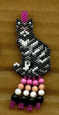 a beaded black and white cat sitting on top of a wooden table next to some beads