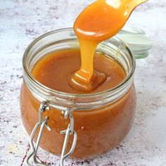 a spoon full of caramel sauce being poured into a jar