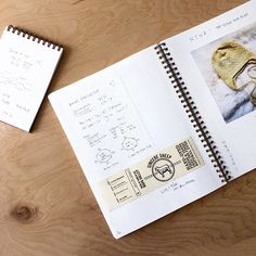 an open notebook on a wooden table next to a pair of eyeglasses and a notepad