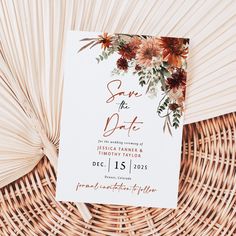 a white save the date card with flowers on it next to a wicker basket