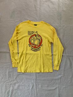 Vintage long sleeve tee with funny graphic and quote, in overall good condition with some faint staining on left sleeve. Fits like a modern Medium Pit to pit 19" Length 26" PLEASE READ! *MEASUREMENTS* All items are measured while laying flat and unstretched. For clothing: chest, waist, hip and thigh measurements should be multiplied by two. All measurements are in inches. *VINTAGE CONDITION* Vintage goods may show signs of wear and age. We always indicate and/or show in pictures any major flaws or blemishes, but will not always mention small flaws, such as pinpoint sized spots or holes. If you are concerned about a particular item's condition, please message us. All of our pieces are pre-owned. We use a natural detergent to wash all our textiles when necessary (with a few exceptions such a Vintage Graphic Print T-shirt For Fall, Vintage Screen Print Tops For Fall, Vintage Screen Printed Tops For Fall, Retro Long Sleeve T-shirt With Screen Print, 90s Long Sleeve Pre-shrunk Tops, 90s Style Long Sleeve Pre-shrunk Top, Vintage Long Sleeve Top With Graphic Print, Vintage Long Sleeve T-shirt With Screen Print, Vintage Yellow T-shirt With Funny Print