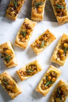 many small pieces of food are arranged on a white surface with rosemary sprigs