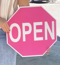 a woman holding a pink and white sign that says open on the side of it