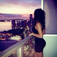 a woman standing on top of a balcony next to a cityscape at night