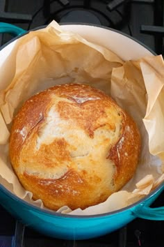 a baked bread in a blue pot on top of an oven burner with wax paper wrapped around it