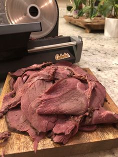 a pile of meat sitting on top of a wooden cutting board next to a machine