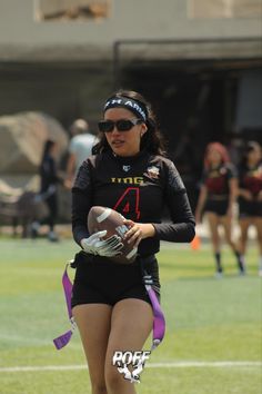 a woman holding a football on top of a field with other people in the background