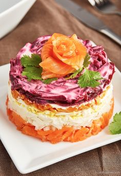 a layered cake with red cabbage and carrots on a white plate next to silverware