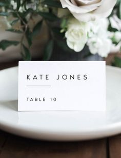 a place card sitting on top of a white plate next to a bouquet of flowers