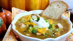 a white bowl filled with soup and topped with sour cream next to two pumpkins