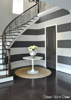 a foyer with black and white stripes painted on the walls, an iron stair case and a round table