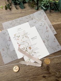 the wedding stationery is laid out on a wooden table next to two gold coins