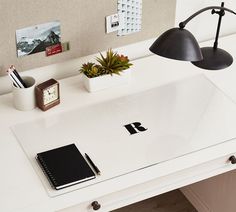 a desk with a laptop, notepad and pen on it next to a lamp