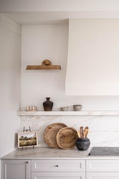 a white kitchen with marble counter tops and shelves above the stove top is filled with cooking utensils