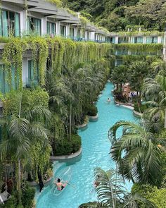 people are swimming in a pool surrounded by trees and plants on the side of a building