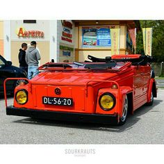 an orange car parked in front of a building with two men standing next to it